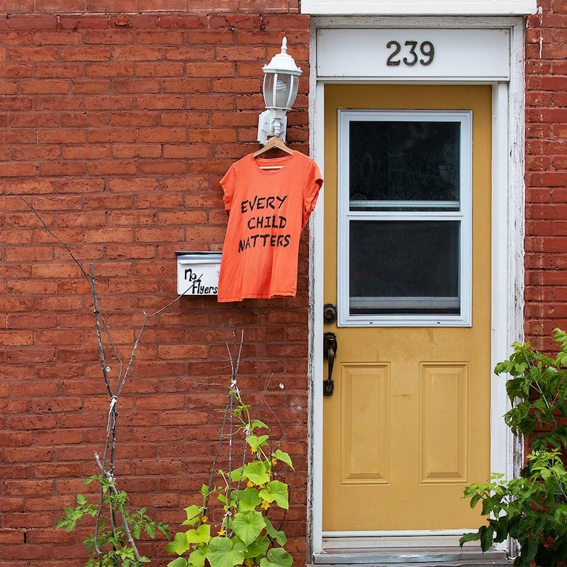 Un chandail orange accroché à une lampe aux côtés d'une porte de maison.