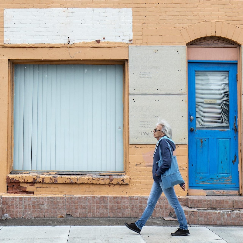 Une femme qui marche vers la gauche devant un édifice qui semble abandonné.