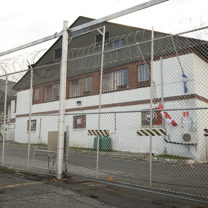 La devanture d'un centre de détention. Une grande clôture recouverte de barbelés se trouve devant l'édifice.