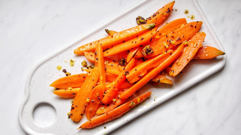 Des carottes glacées au gingembre, graines de moutarde et au miel déposées sur un plateau.