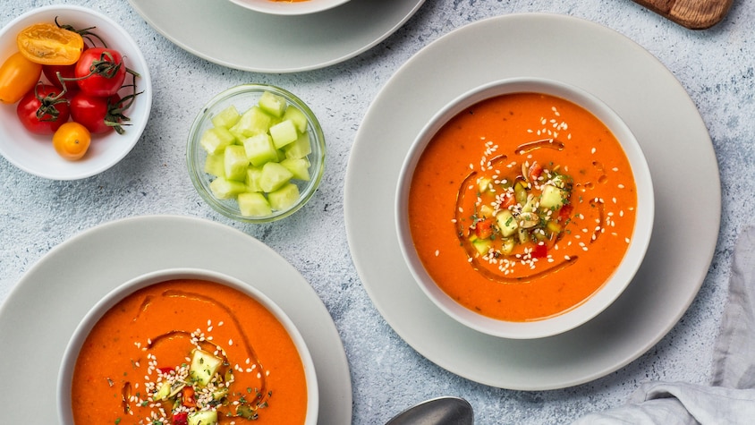 Trois bols de soupe froide aux tomates vu de haut sur une table en marbre.