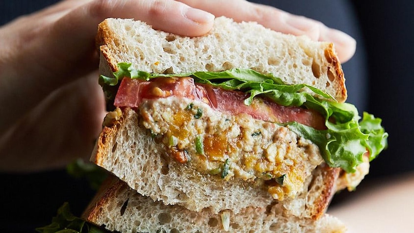 Un sandwich bien garni dans les mains d'une personne.