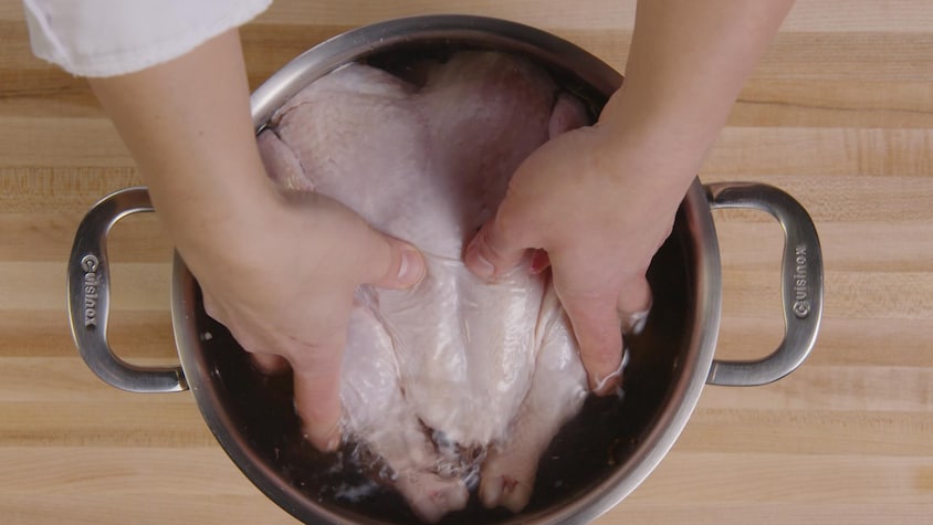 Une personne plonge un poulet cru dans une casserole contenant de la saumure. 