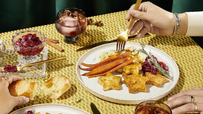 Une table des fêtes avec une assiette de tofu, carottes glacées, purée de pomme de terre et compote de canneberges.