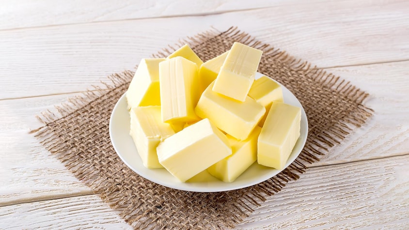 Des carrés de beurre dans une assiette blanche déposée sur une table aspect bois.