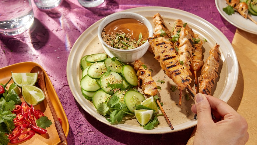 Des brochettes de poulet avec des concombres, de la lime, de la coriandre et une sauce.