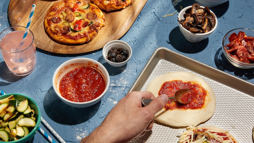 Quelques pizzas garnies sur une planche de bois et des bols de condiments autour. 