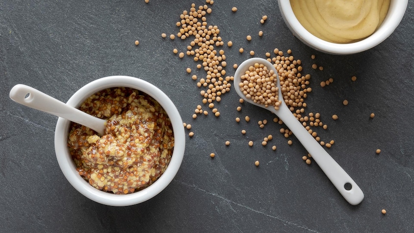 De la moutarde en grains dans un bol et de la moutarde liquide dans un autre.