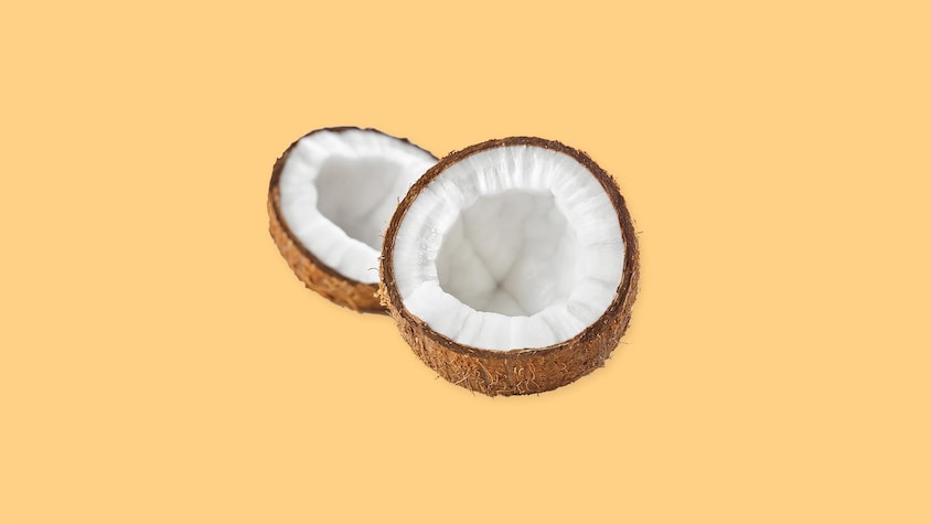 Une noix de coco coupée en deux sur un fond jaune.