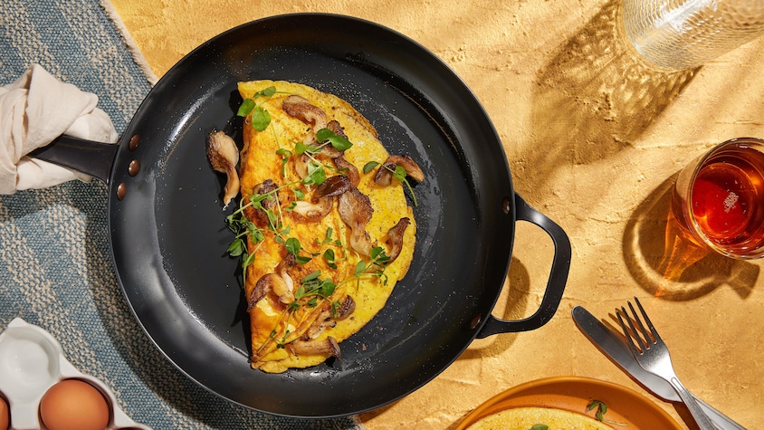 Une omelette recouverte de champignons et de verdure dans une poêle.