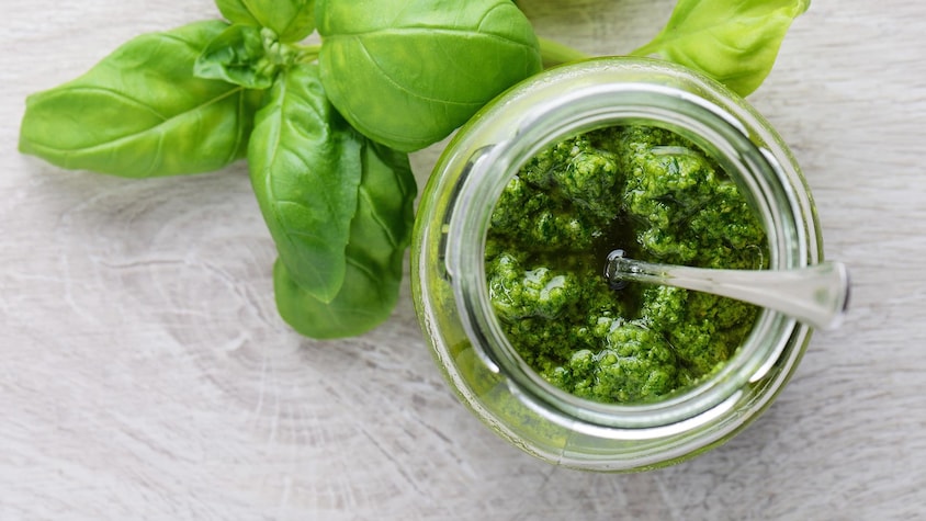 Du pesto dans un bol transparent et des feuilles de basilic frais déposées à côté du bol.