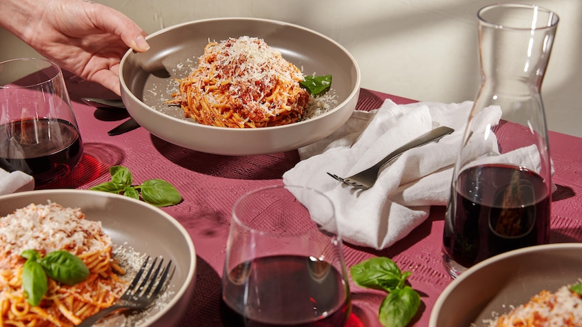 Trois assiettes de spaghetti servies avec du vin rouge.