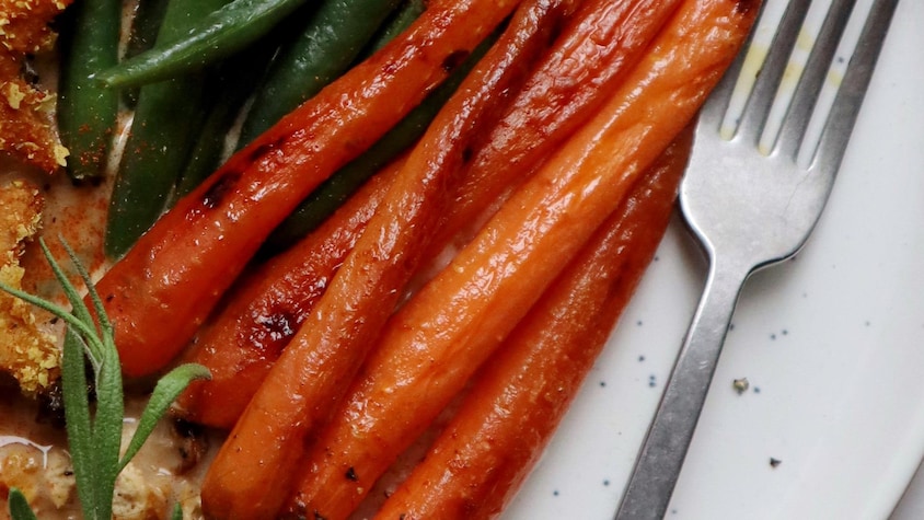 Dans une assiette, il y a des carottes grillées à l'érable avec des petites fèves vertes.