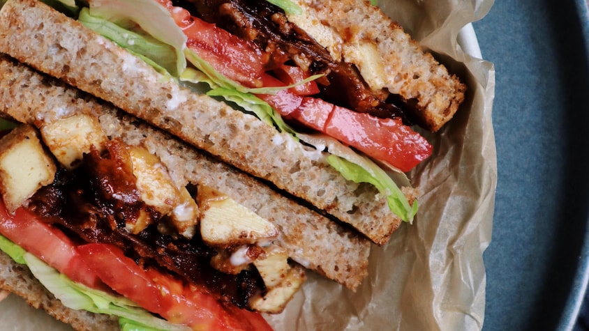Dans une assiette, se trouve un club sandwich au tofu magique.