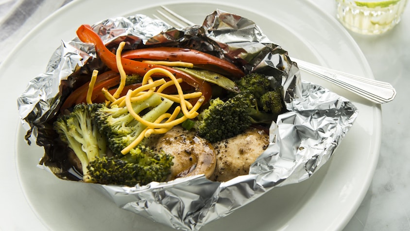 Papillote de poulet avec légumes dans un papier d'aluminium servi dans une assiette.
