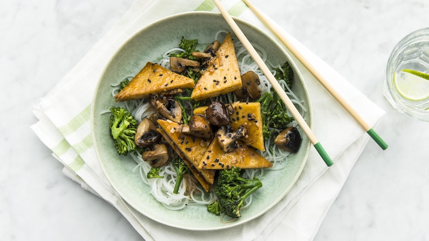 Tofu teriyaki aux champignons et au mini brocolis avec vermicelles de riz dans une assiette avec des baguettes.
