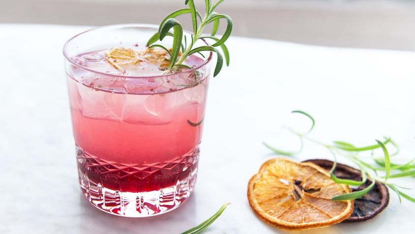 Un verre de gin tonic rose à côte de tranches d’orange sanguine séchée