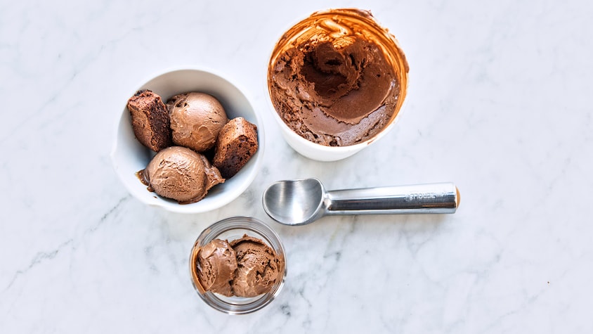 Un bol de crème glacée au chocolat avec un bol rempli, un pot de verre et une cuillère pour la servir.