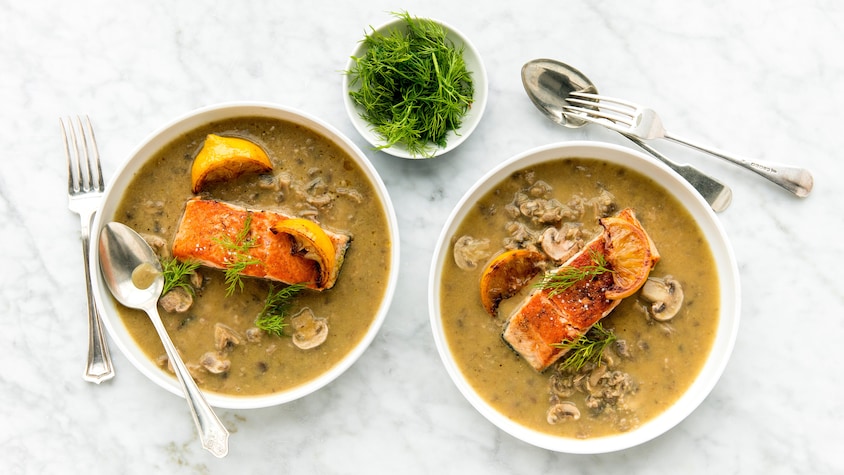 Deux bols de soupe remplis de soupe veloutée aux champignons avec du saumon poêlé sur le dessus.