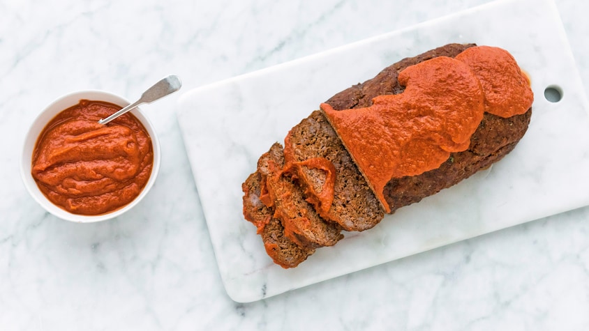Sur une planche à découper, il y a un pain de viande avec de la sauce tomate sur le dessus.