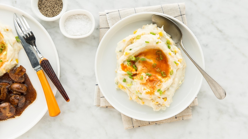 Une petite assiette de purée de pommes de terre au maïs garnie de beurre d'harissa et d'oignons verts.