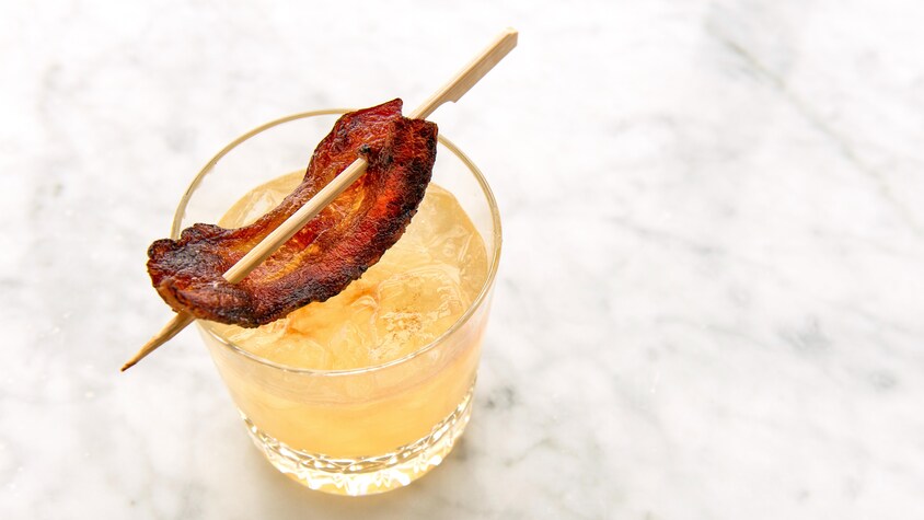 Un verre de whisky sour à l'érable décoré d'une tranche de bacon sur un bâton en bois.