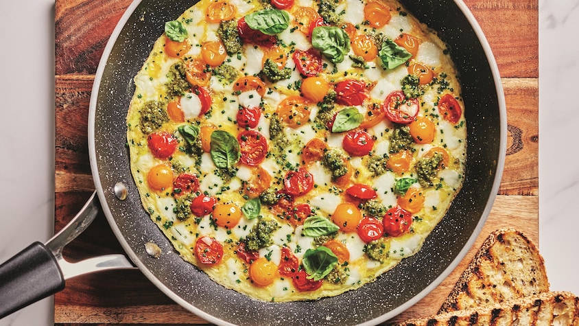 Une omelette aux tomates, mozzarella et pesto dans une poêle.