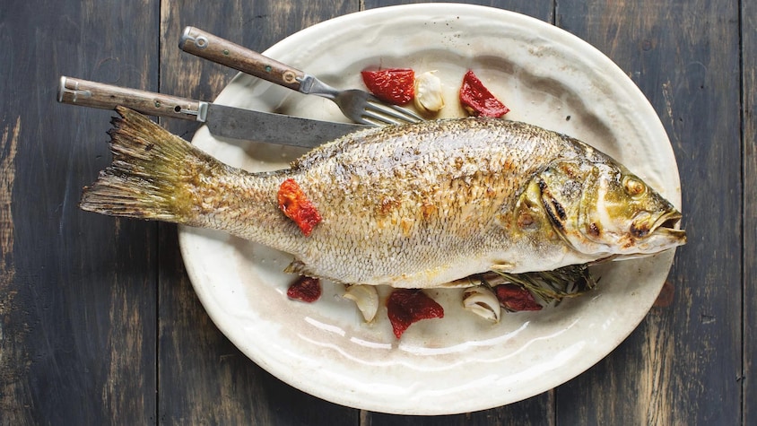 Un poisson entier grillé dans une assiette ovale.