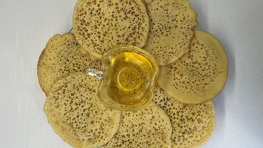 Des petites crêpes disposées dans une assiette avec un petit pot de miel au centre.