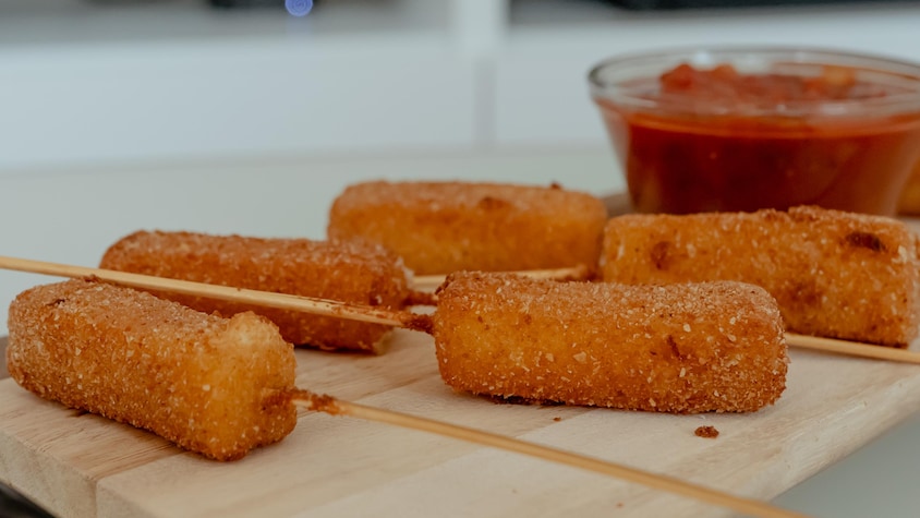 Des bâtonnets de fromage frits sur une planche de service avec un bol de sauce.