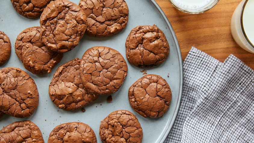 Biscuits brownies dans une grande assiette de service sur une table en bois avec un linge de table et un verre de lait.