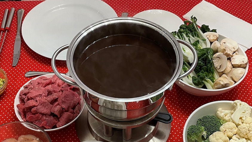 Un plat à fondue chinoise rempli de bouillon entouré de diverses sauces et de viande à fondue.