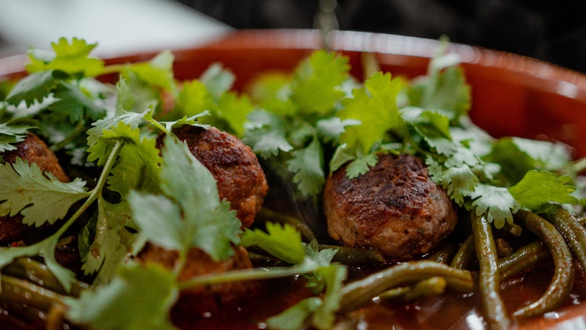 Des boulettes, des haricots verts et de la coriandre dans un bol.