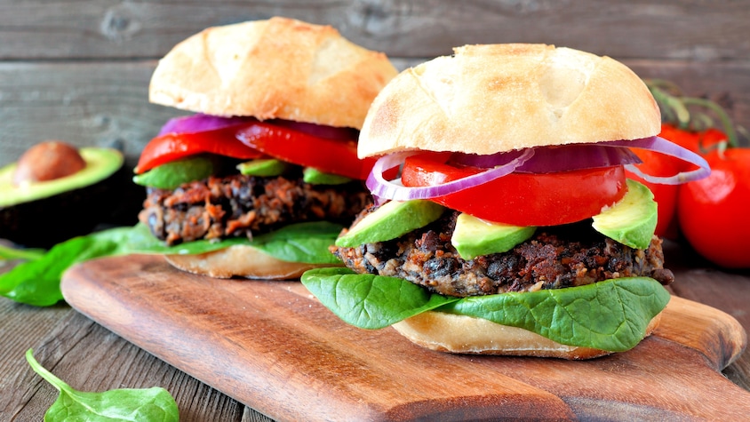 Deux burgers aux fèves noires sur une planche en bois.
