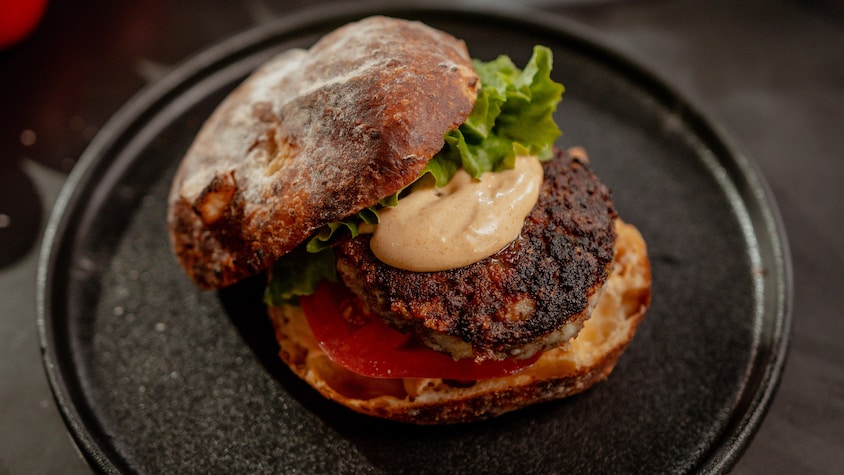 Un burger garni de laitue, d'une tranche de tomate, d'une boulette de viande et de sauce dans une assiette noire.