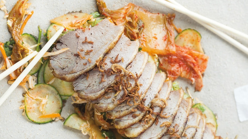 Des tranches de canard laqué dans une assiette de service accompagnées de kimchi.