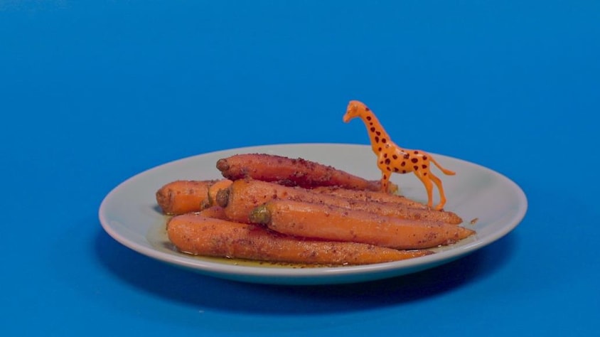 Une assiette de carottes glacées, sur lesquelles se repose une petite girafe de plastique orange.