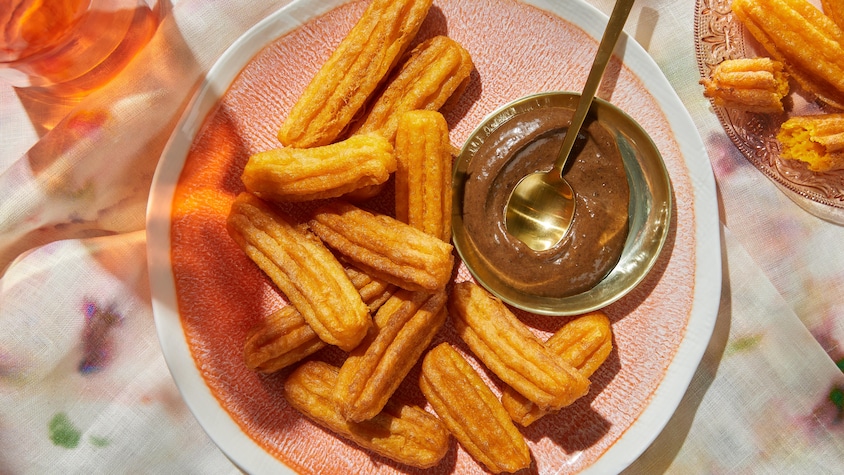 Des churros aux carottes sont disposés dans une assiette avec un petit bol de mayonnaise à l'ail noir.