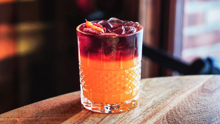 Un cocktail avec le fond orangé et le dessus rouge vin. 