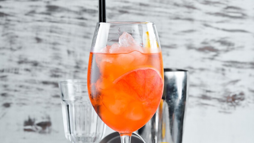 Un cocktail orange dans une coupe de vin, un demi-pamplemousse, un mélangeur à cocktail.