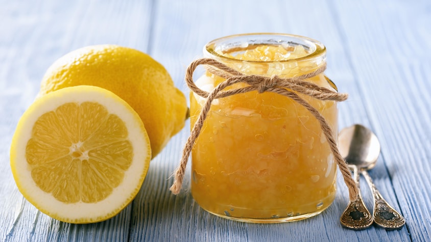 Un pot de marmelade aux côtés d'une citron entier et d'un demi-citron.