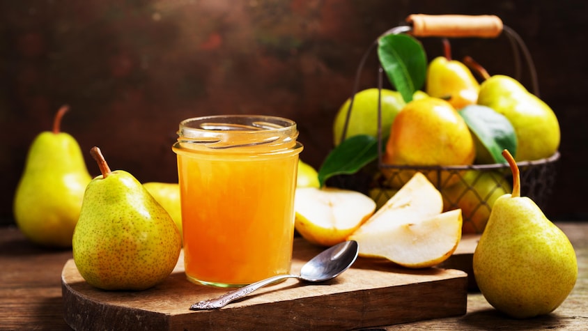 Un pot de confiture de poires sur une planche de bois, avec des poires entières et tranchées.