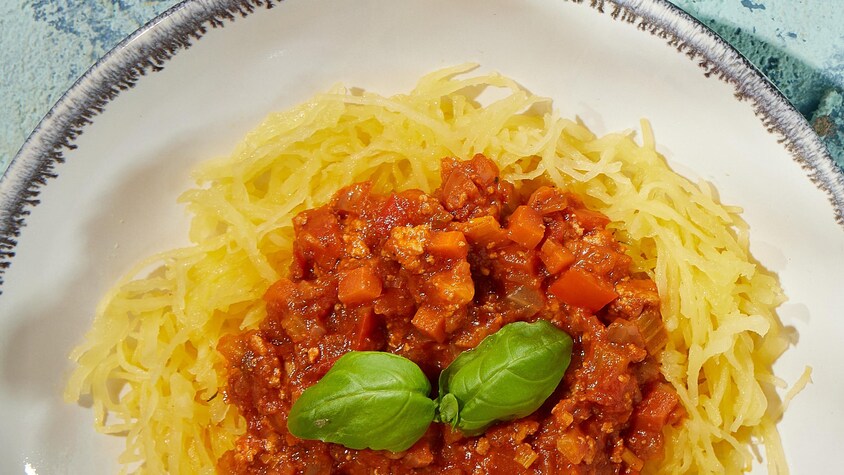 Courge spaghetti garnie de sauce bolognaise et de feuilles de basilic.