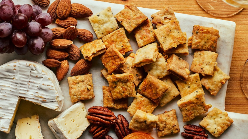 Une planche apéro garnie de craquelins au fromage, raisins frais, abricots secs, noix et brie. 