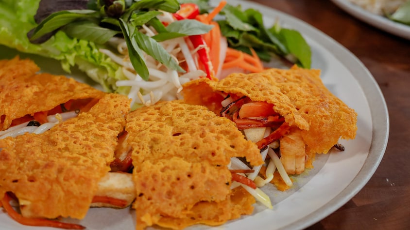 Des tranches de crêpes vietnamiennes farcies, accompagnées d'herbes fraîches, de légumes marinés et de fèves germées.