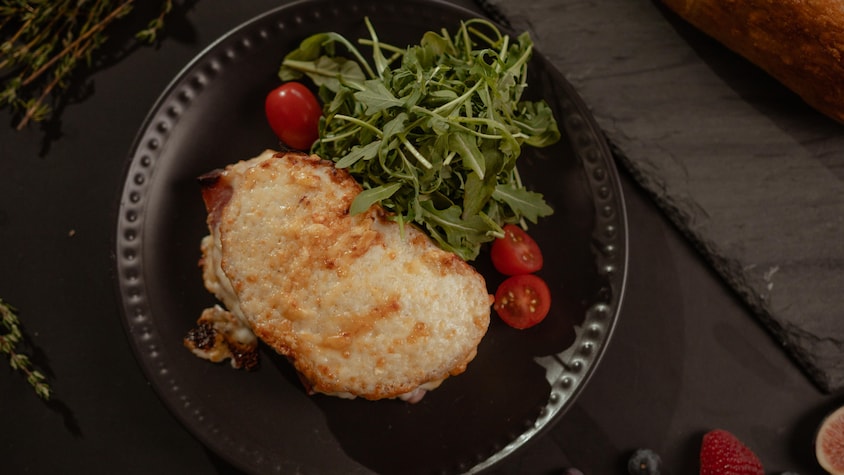 Un croque-monsieur dans une assiette noire avec de la roquette et des tomates cerises.