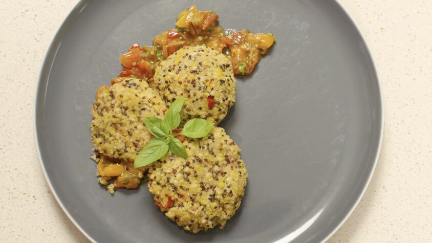 Trois croquettes de quinoa dans une assiette avec un peu de concassé de tomates cerises et de pesto.