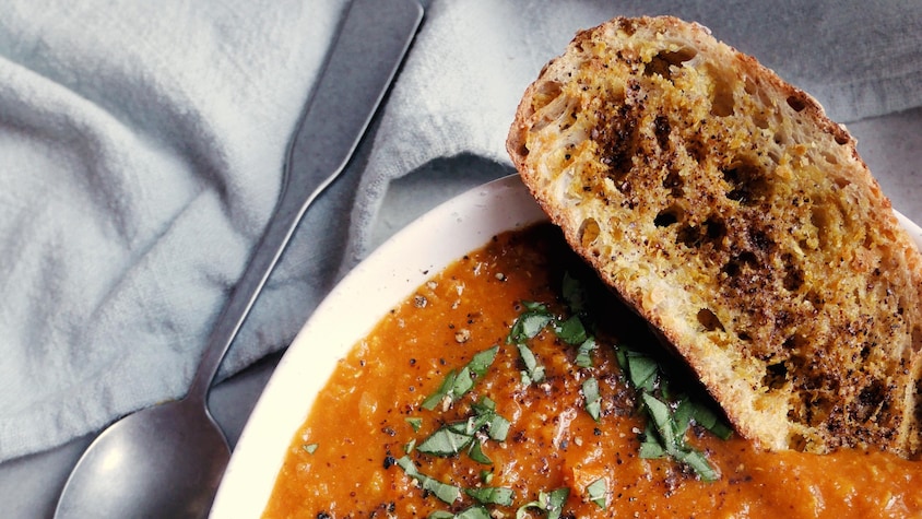 Vue en plongée sur un bol de soupe de lentilles avec un croûton trempant dans la soupe et une cuillère posée à côté du bol.