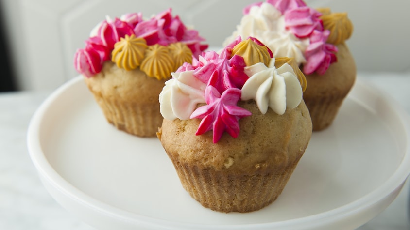 Trois cupcakes à la vanille avec du glaçage, servis sur un piédestal à gâteau.