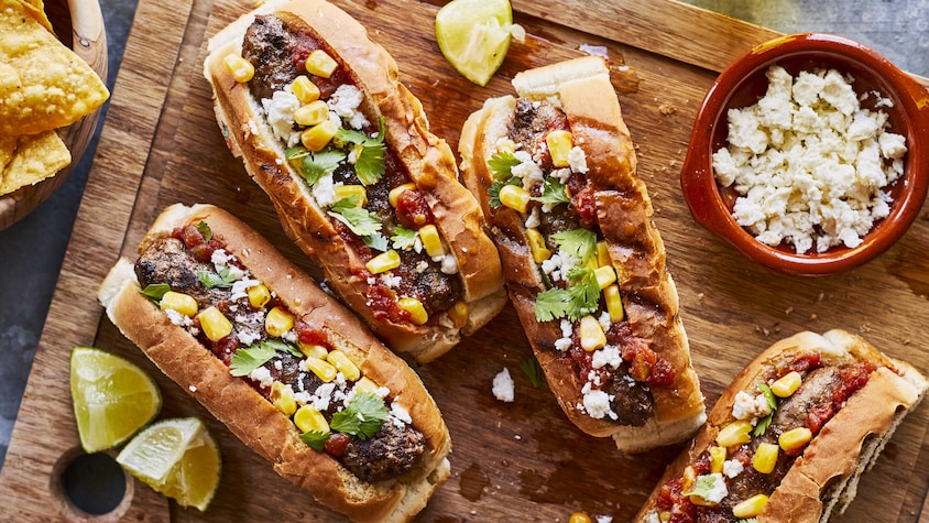 Quatre dogburgers à la mexicaine sur une planche de bois.